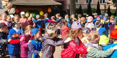 Powiększ grafikę: W ogrodzie przedszkolnym odbywa się festyn. Dzieci ustawione w "pociąg" biorą udział w zabawie.
