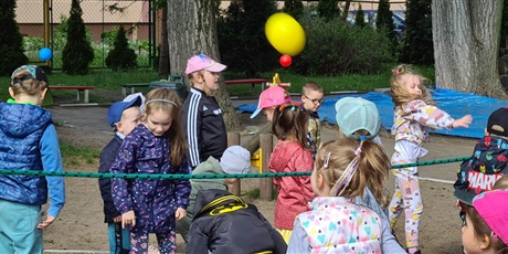 Powiększ grafikę: W ogrodzie przedszkolnym odbywa się festyn. Dzieci biorą udział w zabawie polegającej na przerzucaniu piłek przez rozciągnięty między nimi sznur.