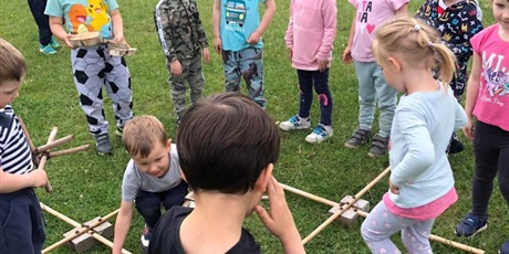 Powiększ grafikę: Dzieci biorą udział w zabawie na świeżym powietrzu. Ich zadaniem jest przejść trasę ułożoną z drewnianych patyków.